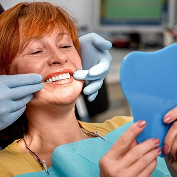 A woman looking in a mirror at her dentures at the dentist’s office