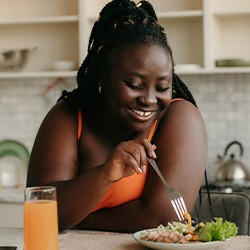 Woman smiling while eating healthy meal in kitchen