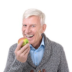 An older man about to bite into an apple