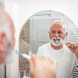 An older man brushing his teeth in the mirror
