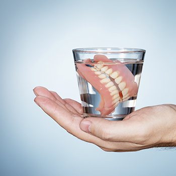 Hand holding a dentures in a glass of soaking solution