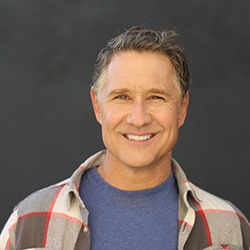 Man smiling wearing a blue t shirt and plaid flannel