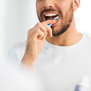 Man smiling while brushing his teeth in bathroom