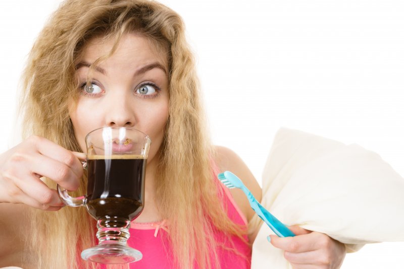 a woman drinking coffee while holding a toothbrush and a pillow